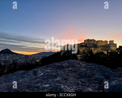 Lever de soleil sur la colline d'Areopagus avec la lumière chaude du matin illuminant l'Acropole et le paysage urbain d'Athènes. Banque D'Images