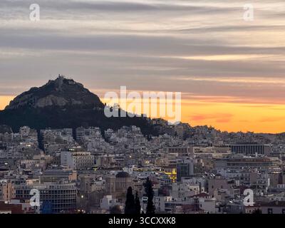 Vue du lever du soleil depuis la colline d'Areopagus avec le paysage urbain d'Athènes, mettant en valeur le bâtiment jaune et la montagne lointaine. Banque D'Images