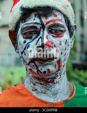 Narayanganj, Bangladesh - 23 août 2019 : vue d'un visage d'homme peint avec des couleurs vives et des motifs complexes, portant un chapeau festif, un portrait captivant. Banque D'Images