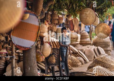 Bogura, Bangladesh - 27 février 2024 : vue d'un garçon local debout au milieu d'une exposition vibrante de produits artisanaux en bambou et en rotin, mettant en valeur le riche patrimoine culturel de la région. Banque D'Images