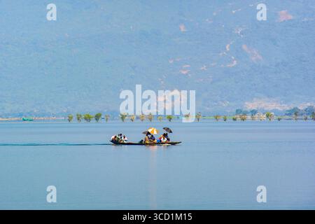 Bogura, Bangladesh - 02 novembre 2017 : vue d'un bateau étroit traditionnel transportant des passagers, glissant à travers les eaux sereines et réfléchissantes sous un ciel doux et brumeux, vers la rive lointaine. Banque D'Images