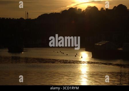 Un coucher de soleil serein sur un plan d'eau, avec bateaux et bouées visibles. Le ciel est une couleur dorée chaude, qui se reflète sur la surface de l'eau. Banque D'Images