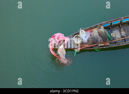 Rangpur, Bangladesh - 02 décembre 2019 : vue aérienne d'un pêcheur solitaire dans un bateau en bois altéré, jetant son filet dans les eaux tranquilles et vertes de jade, une scène d'industrie tranquille. Banque D'Images