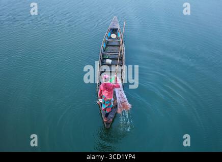 Rangpur, Bangladesh - 02 décembre 2019 : vue aérienne d'un pêcheur solitaire jetant son filet depuis un bateau élancé sur les eaux tranquilles et chatoyantes d'une rivière, des ondulations se propageant vers l'extérieur. Banque D'Images
