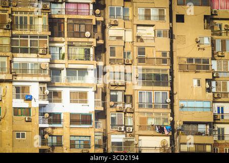 Vue d'appartements étroitement emballés empilés haut, fenêtres reflétant la lumière du soleil, avec des unités de climatisation accrochées à la façade altérée, le Caire, gouvernorat de Gizeh, Egypte. Banque D'Images