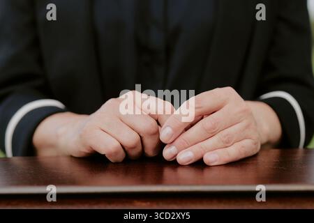 Femme caucasienne d'âge moyen serrant les mains sur la surface en bois pendant la cérémonie funéraire, doigts doucement entrelacés, portant une tenue formelle, geste solennel reflétant le deuil et le souvenir Banque D'Images