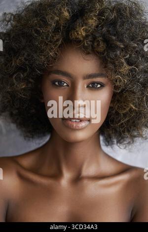 Rognez une jeune femme ethnique avec des cheveux bouclés en regardant l'appareil photo sur un arrière-plan flou Banque D'Images