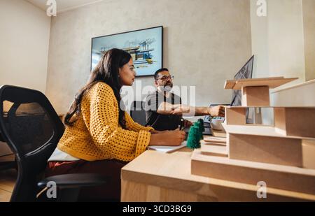 Deux individus engagés dans un projet collaboratif dans un bureau lumineux, représentant un cadre moderne et ciblé de cabinet d'architecture. Banque D'Images