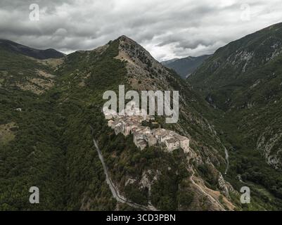 Vue aérienne d'un ancien village accroché à une crête précipitée, embrassé par des pentes verdoyantes sous un ciel couvant, Castrovalva, Abruzzes, Italie. Banque D'Images