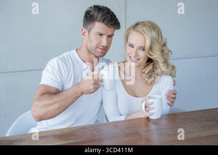 Attrayant homme aimant et femme assis prenant le café du matin avec le bras de maris autour de ses épaules de veuves Banque D'Images