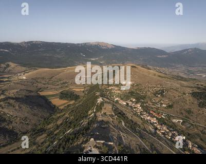 Vue aérienne de l'ancien village forteresse accroché à la crête, une tapisserie de pierre ocre contre les pics accidentés des Apennins, Rocca Calascio, Abruzzes, Italie. Banque D'Images