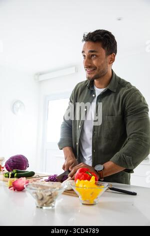 Homme du moyen-Orient hachant des légumes à l'îlot de cuisine sur la planche à découper avec le couteau du chef Banque D'Images