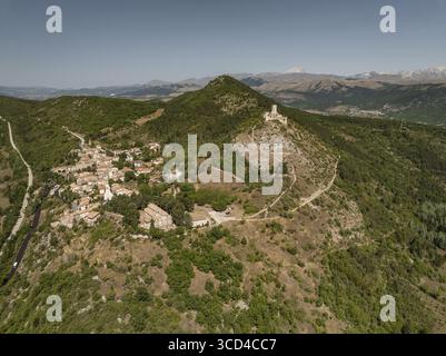 Vue aérienne d'un village médiéval niché sur une colline avec une ruine de château perché au sommet, une tapisserie de feuillage vert contrastant avec la pierre chaude, Caporciano, Abruzzes, Italie. Banque D'Images