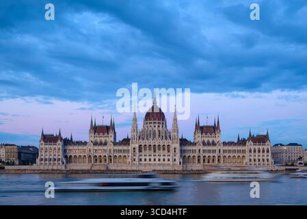 Le majestueux bâtiment du Parlement hongrois se dresse le long du Danube alors que le ciel passe au crépuscule. Les bateaux glissent devant, reflétant l'emblématique Banque D'Images
