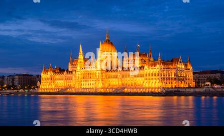 Le majestueux bâtiment du Parlement hongrois est illuminé contre le ciel sombre, reflétant magnifiquement sur le Danube à Budapest pendant Banque D'Images