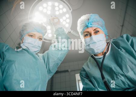 Deux femmes chirurgiennes en gommages et masques, se préparent à la chirurgie sous les lumières lumineuses de la salle d'opération, mettant l'accent sur la collaboration et le dévouement dans un M. Banque D'Images