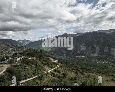 Vue aérienne de l'ancien village accroché à la colline, une tapisserie de pierre et de vert surplombant le lac tranquille et les montagnes lointaines, Frattura Vecchia, Scanno, Abruzzes, Italie. Banque D'Images
