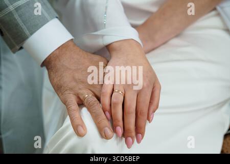Un gros plan montre des alliances échangées sur les mains d'une mariée et d'un marié, symbolisant l'amour. les tenues de mariage blanches ajoutent de l'élégance Banque D'Images