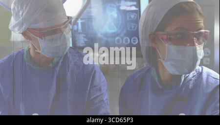 Chirurgiennes portant des vêtements chirurgicaux surveillant les acquisitions sur le moniteur au BLOC OPÉRATOIRE, avec une lampe chirurgicale Banque D'Images