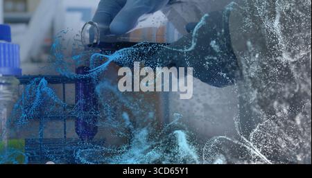 Mains gantées pipetage de liquide violet dans un portoir pour tubes à essai en laboratoire, superposition numérique Banque D'Images