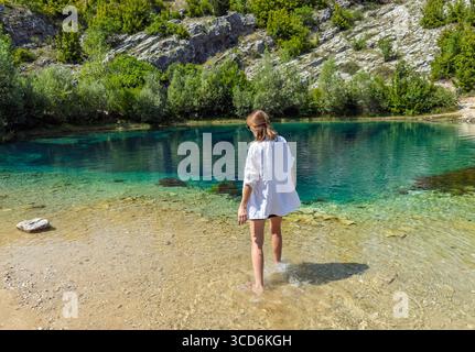 Femme dans une chemise blanche apprécie la nature immaculée, pataugant pieds nus dans le lac de montagne cristalline Eye of the Earth of the Cetina River Spring in Banque D'Images