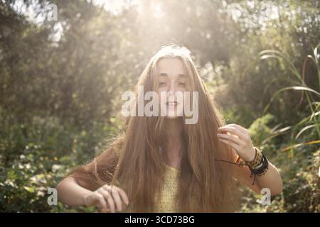 Boho fille avec de longs cheveux blonds posant devant de hauts arbres dans un parc couleur rétro éclairé par LED shot Banque D'Images
