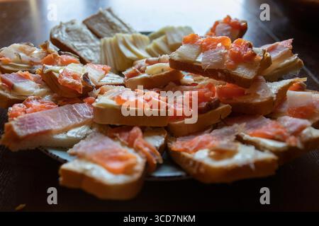 Vue de dessus de sandwichs ouverts assortis avec poisson salé, bacon et beurre sur des tranches de pain, accompagnés de fromage. Apéritif maison rustique, p Banque D'Images