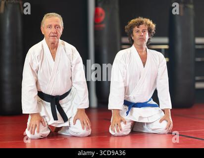 Hommes en kimono assis à genoux sur tatami dans la salle de gym Banque D'Images