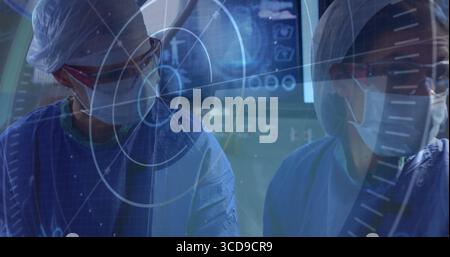 Examen des acquisitions deux chirurgiens portant des blouses chirurgicales et des masques dans la salle d'opération, avec des moniteurs Banque D'Images