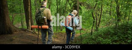 Homme et femme caucasien senior randonnée avec des sacs à dos à travers Forest Trail Banque D'Images