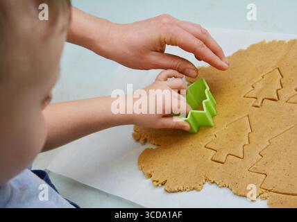 Gros plan sur un enfant en bas âge faisant des desserts de biscuits de vacances, boulangerie de pain d'épice de noël, découpe des figures de sapin de la pâte roulée avec h de la mère Banque D'Images