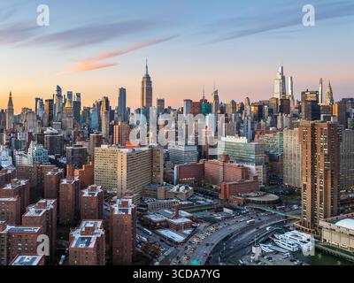 Vue aérienne de l'horizon avec l'Empire State Building perçant le ciel, une tapisserie de béton et de verre captant les teintes chaudes du soleil couchant, New York, New York, États-Unis. Banque D'Images
