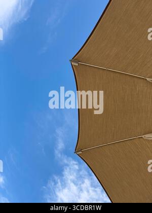 Parasol beige couvrant partiellement le ciel bleu avec quelques nuages, offrant ombre et protection contre le soleil Banque D'Images