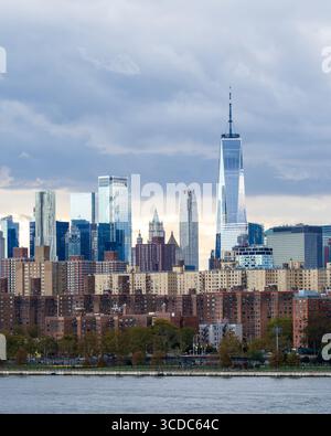 Vue des gratte-ciel frappants de Manhattan perce le ciel nuageux, s'élevant au-dessus des immeubles d'appartements bruns près d'une rivière un jour d'automne, New York, New York Banque D'Images