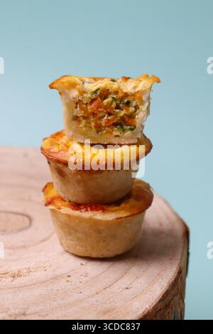 tour de 3 mini quiches végétales sur une surface en bois et un fond vert menthe. Une des mini quiches est coupée ouverte, montrant la garniture de légumes Banque D'Images