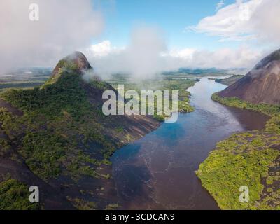 Vue aérienne de la rivière sombre serpentant entre les rives verdoyantes et l'imposant Cerros Mavicure, embrassé par les nuages, Puerto Inírida, Cerros Mavicure, Colombie. Banque D'Images
