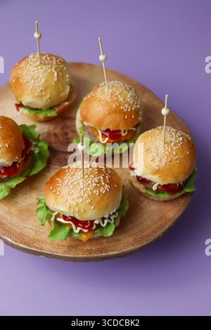 Une vue de haut en bas d'un plateau de service en bois avec plusieurs mini hamburgers ou sliders, garni de laitue et de fromage, et tenu avec des cure-dents Banque D'Images