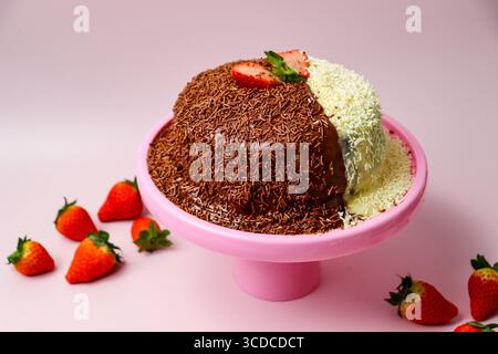 Gâteau éponge riche recouvert de crème glacée au chocolat blanc et au lait avec des saupoudres. Décoré de fraises fraîches. Stand de gâteau rose et fond Banque D'Images