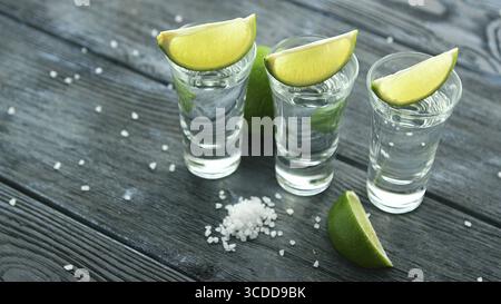 Rangée de perles en verres de tequila et vert lime slices aigre sur table en bois avec des tas de sel Banque D'Images