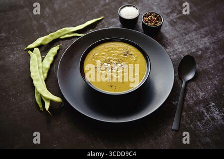 Nourriture saine. Soupe crémeuse aux haricots verts dans un bol noir en céramique sur une table rustique sombre. Le concept de régime alimentaire Banque D'Images