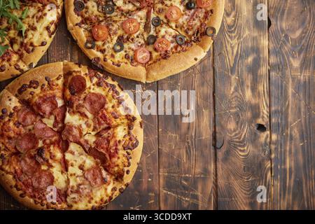 Composition de trois pizzas de différentes sortes placées sur une table en bois rayé rouillé. Nourriture chaude et fraîche prête à manger Banque D'Images