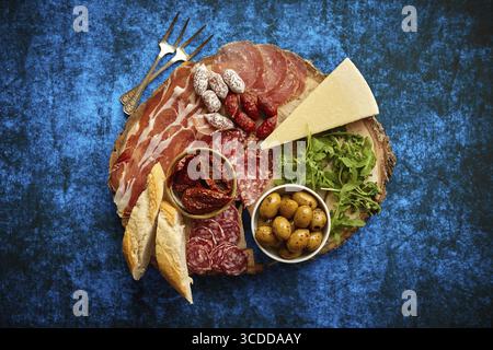 Délicieux mélange de différentes collations et hors-d'œuvre. Tapas espagnoles ou antipasti italiens sur une assiette en bois. Vue de dessus. Placé sur la table bleue Banque D'Images