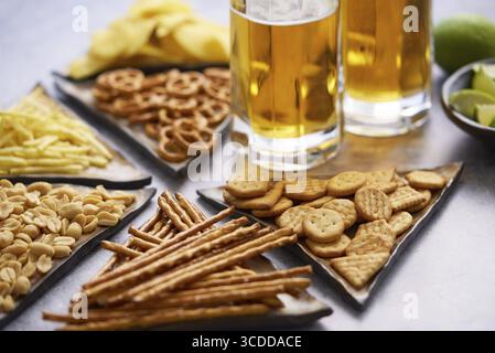 Gros plan de deux verres de bière avec divers en-cas assortis. Comme les frites, les craquelins, les bretzels, les arachides, les frites Banque D'Images