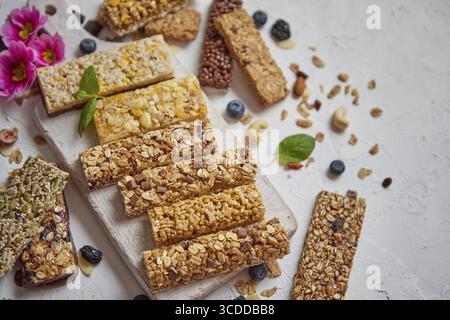 Différents types de barres granola protéinées avec des fruits secs et des baies. Placé sur une planche à découper en bois blanc. Plat, vue de dessus Banque D'Images
