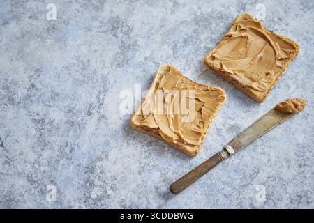 Deux savoureux toasts au beurre d'arachide placés sur une table en pierre. Couteau sur le côté. Prise de vue en angle supérieur avec espace de copie Banque D'Images