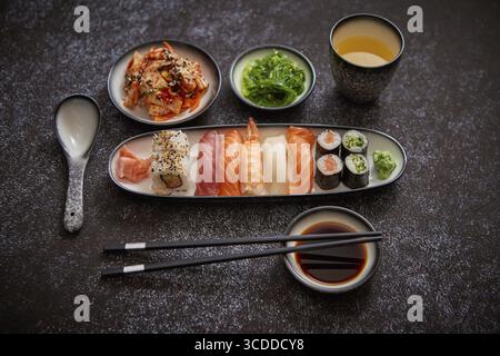 Assortiment de plats asiatiques. Divers rouleaux de sushi placés sur des plaques en céramique. Salades de kimchi et de wakame de goma. Soupe soja et baguettes sur les côtés. bac noir grungy Banque D'Images