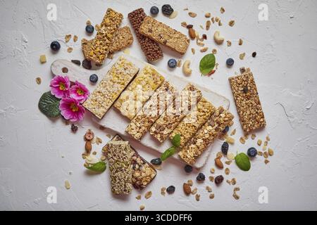 Différents types de barres granola protéinées avec des fruits secs et des baies. Placé sur une planche à découper en bois blanc. Pose à plat avec espace de copie Banque D'Images