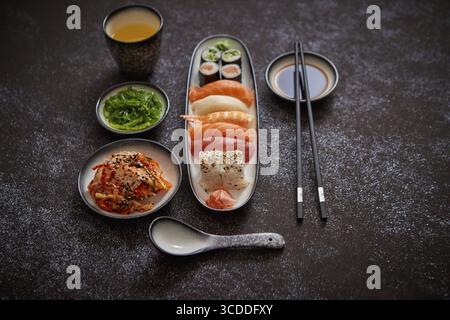 Assortiment de plats asiatiques. Divers rouleaux de sushi placés sur des plaques en céramique. Salades de kimchi et de wakame de goma. Soupe soja et baguettes sur les côtés. bac noir grungy Banque D'Images