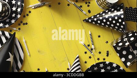 De la vue de dessus des chapeaux et des assiettes en papier décoratif dans les couleurs noir et blanc posés en cercle sur fond de bois jaune Banque D'Images