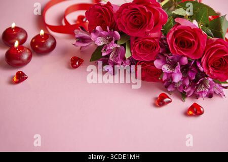 Bouquet de fleurs mixtes avec des roses, des bougies et de l'acrylique en forme de coeur décorations sur fond rose. Cadeau pour la Saint-Valentin, le 8 mars ou date romantique. Banque D'Images
